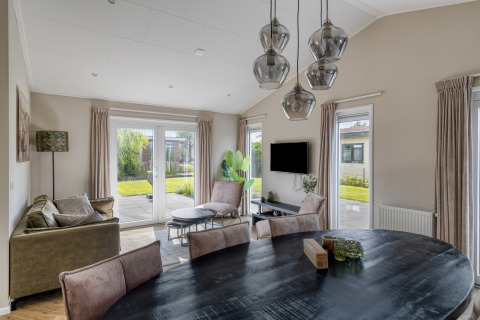 Salon moderne d’un lodge Natuurhoeve du parc Westerkogge aux Pays-Bas, avec vue sur jardin à travers de grandes fenêtres.