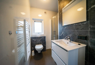 Baño moderno con inodoro suspendido, lavabo y espejo en la cabaña Pavilion 4+4 en EuroParcs Texel, Países Bajos.