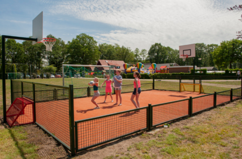 Children play on a multi-sports court with basketball hoops at Camping Goorzicht, North Holland, Netherlands.