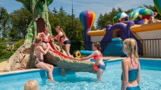 Bambini giocano in piscina con scivolo e gonfiabili al campeggio Goorzicht nei Paesi Bassi.