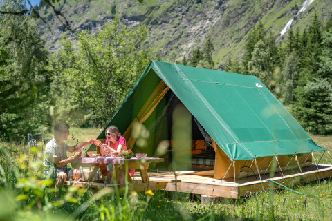 Zwei Personen genießen ein Picknick vor einem luxuriösen Zelt bei Huttopia Vanoise in Auvergne-Rhône-Alpes.