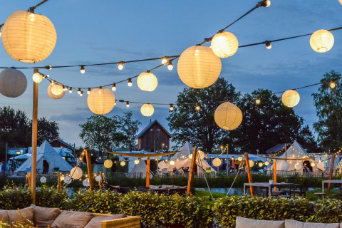 Noche en Holiday Park Mölke en Overijssel, Países Bajos, con luces colgantes y tiendas de fondo.