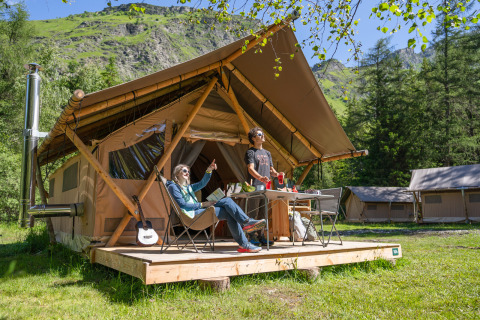 Deux personnes profitent du glamping devant une tente de luxe à Huttopia Vanoise en Auvergne-Rhône-Alpes.