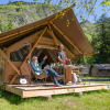 Two people enjoying glamping in front of a luxury tent at Huttopia Vanoise in scenic Auvergne-Rhône-Alpes.