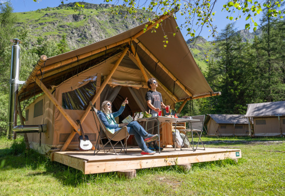 Deux personnes profitent du glamping devant une tente de luxe à Huttopia Vanoise en Auvergne-Rhône-Alpes.