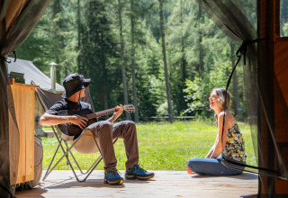 Dos personas disfrutan glamping en Huttopia Vanoise – Champagny, Auvernia-Ródano-Alpes; uno toca la guitarra.