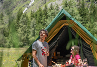 Deux personnes profitent du glamping devant une tente dans les montagnes vertes d’Huttopia Vanoise – Champagny.