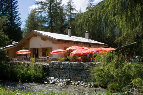 Glamping Huttopia Vanoise – Champagny in Auvergne-Rhône-Alpes con ombrelloni rossi e natura circostante.