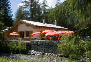 Glamping Huttopia Vanoise – Champagny in Auvergne-Rhône-Alpes con ombrelloni rossi e natura circostante.