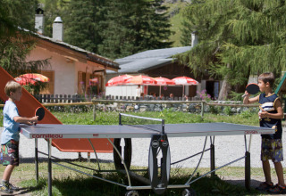 Deux enfants jouent au tennis de table en plein air à Huttopia Vanoise – Champagny glamping, Auvergne-Rhône-Alpes.