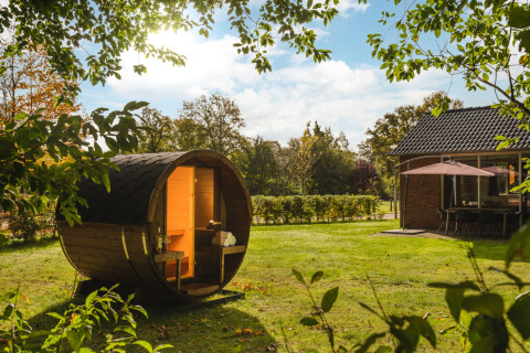 Una sauna de barril en el jardín soleado del Holiday Park Mölke, Overijssel, Países Bajos, junto a una cabaña.