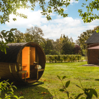 Een barrelsauna in de zonnige tuin van Holiday Park Mölke, Overijssel, Nederland, met een huisje op de achtergrond.