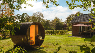 Una sauna de barril en el jardín soleado del Holiday Park Mölke, Overijssel, Países Bajos, junto a una cabaña.