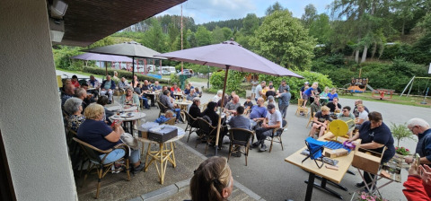 Mennesker nyder udendørs aktiviteter og samvær under paraplyer på Camping Reiler i Luxembourg.