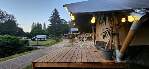 Holzterrasse mit Lichterkette im Camping Reiler, einem Ferienpark im Kanton Clerf, Luxemburg, mit Wohnmobil.