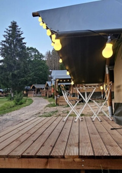 Terrasse en bois illuminée au Camping Reiler, parc de vacances à Clervaux, Luxembourg, avec camping-car en arrière-plan.