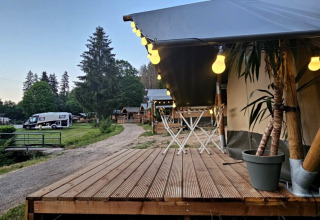 Holzterrasse mit Lichterkette im Camping Reiler, einem Ferienpark im Kanton Clerf, Luxemburg, mit Wohnmobil.