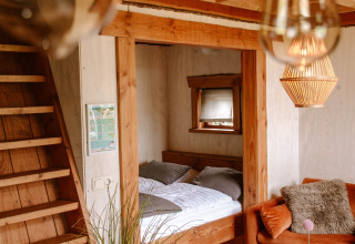 Hyggelig indretning i træhytte på Holiday Park Mölke i Overijssel, Holland med seng, sofa og loft.