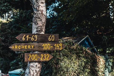 Houten wegwijzers bij Camping Reiler in Luxemburg, wijzen naar boogschieten en kamernummers.