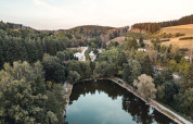 Aerial view of Camping Reiler in Canton Clervaux, Luxembourg, showing a serene pond and lush forest.