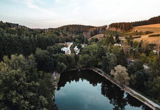 Vista aérea de Camping Reiler en Cantón Clervaux, Luxemburgo, con estanque, bosques y casas de vacaciones.