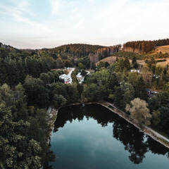 Vue aérienne du Camping Reiler dans le canton de Clervaux, Luxembourg, avec étang et forêt verdoyante.
