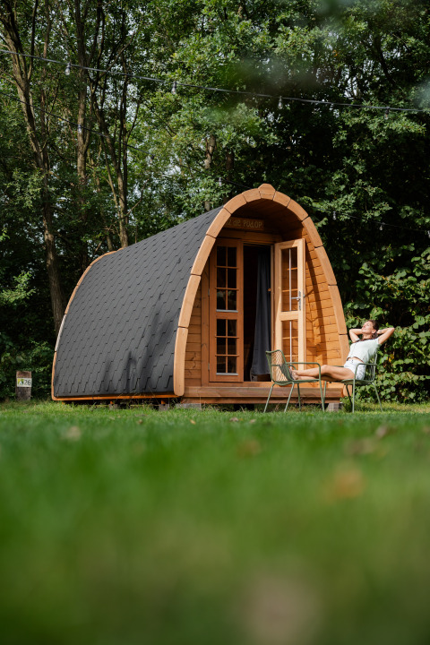 Eine Person entspannt vor einer Duo Panorama pød, einer kleinen Holzhütte inmitten grüner Natur und Bäumen.