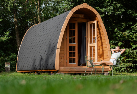 Eine Person entspannt vor einer Duo Panorama pød, einer kleinen Holzhütte inmitten grüner Natur und Bäumen.