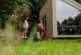 Two women arrive at the Luxe & Lazy Lodge tiny house at RØSTIG Dorst, Netherlands, surrounded by nature.