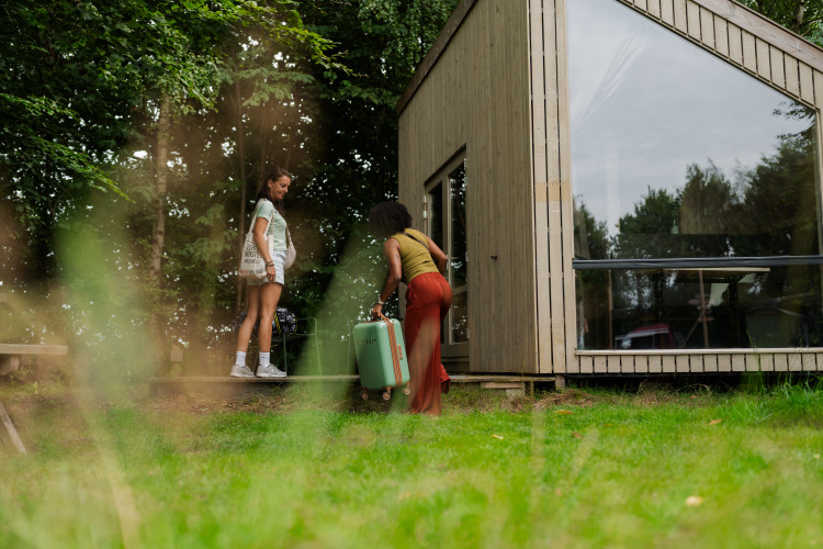 Dos mujeres llegan a la tiny house Luxe & Lazy Lodge en RØSTIG Dorst, Países Bajos, rodeadas de naturaleza.