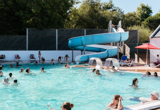 Piscine extérieure au Flower Camping Le Kerarno, Bretagne, familles nageant et toboggan bleu visible.