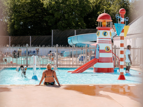 Niños juegan en la piscina con tobogán y faro en Flower Camping Le Kerarno, un parque vacacional en Bretaña, Francia.
