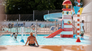 Bambini giocano in piscina con scivolo e faro a Flower Camping Le Kerarno, parco vacanze in Bretagna, Francia.