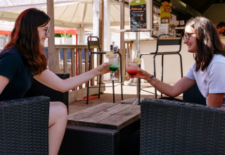 Twee vrouwen klinken met kleurrijke drankjes op het terras van Flower Camping Le Kerarno in Bretagne, Frankrijk.