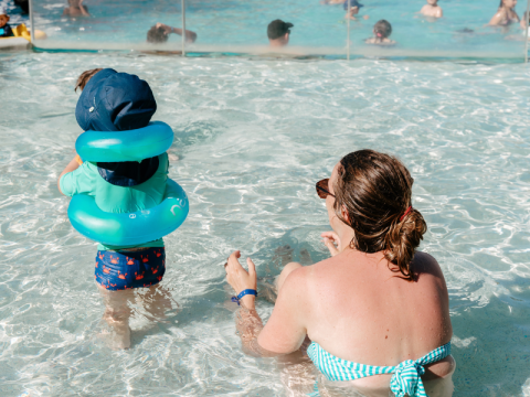 Enfant avec bouée et adulte dans la piscine de Flower Camping Le Kerarno, parc de vacances en Bretagne, France.