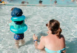 Kind mit Schwimmhilfe und erwachsener Begleitung im Pool bei Flower Camping Le Kerarno, Bretagne, Frankreich.