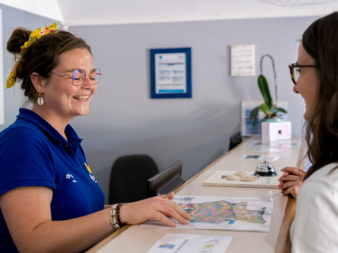 Receptionist sorridente aiuta un ospite con una mappa al Flower Camping Le Kerarno in Bretagna, Francia.