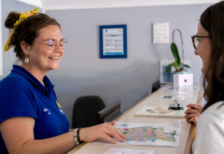 Receptionist smiling while assisting a guest with a map at Flower Camping Le Kerarno, Brittany, France.