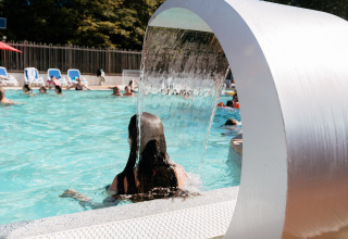 Persona sotto una cascata d’acqua nella piscina esterna del Flower Camping Le Kerarno in Bretagna, Francia.