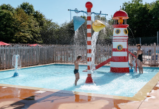 Bambini giocano in una piscina bassa con parco giochi d'acqua e scivolo a Flower Camping Le Kerarno, Francia.