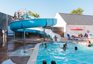 Familias disfrutan junto a la piscina y un gran tobogán azul en Flower Camping Le Kerarno en Bretaña, Francia.