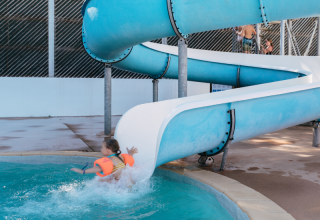 A child with orange armbands splashes into the pool from a blue water slide at Flower Camping Le Kerarno, Brittany.