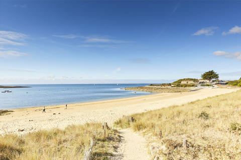 Sandy beach and calm blue sea near Saint-Philibert, Brittany, France, with a few people walking along.