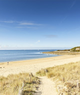 Spiaggia sabbiosa e mare calmo vicino a Saint-Philibert, Bretagna, Francia, con poche persone che camminano.