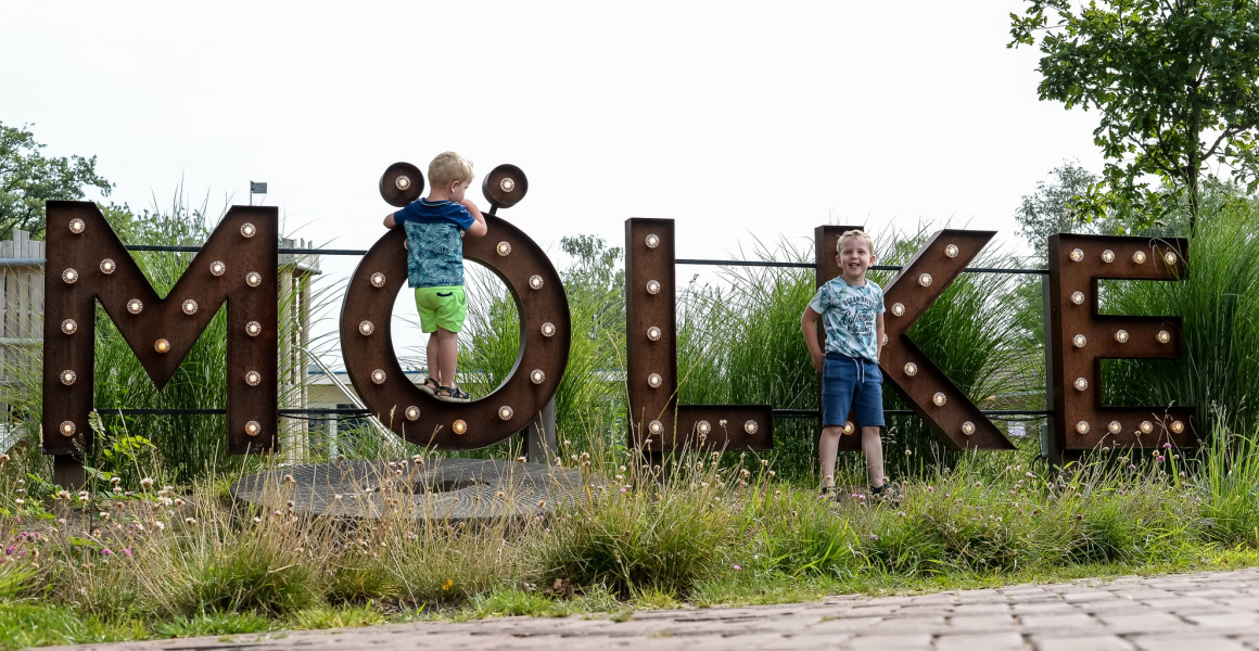 Twee kinderen spelen bij het grote 'MÖLKE'-bord in vakantiepark Mölke in Overijssel, Nederland.