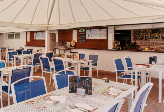 Openlucht eetruimte met blauwe stoelen en witte tafels op Flower Camping Le Kerarno, Bretagne, Frankrijk.