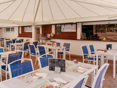 Zona de comedor al aire libre con sillas azules y mesas blancas en Flower Camping Le Kerarno, Bretaña, Francia.
