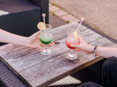 Twee mensen proosten met kleurrijke cocktails met citroen bij Flower Camping Le Kerarno in Bretagne, Frankrijk.