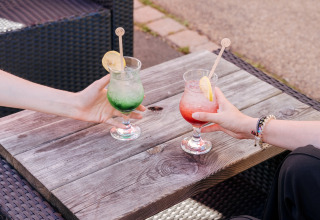 To personer holder farverige cocktails med citron på en træbord i Flower Camping Le Kerarno, Bretagne, Frankrig.