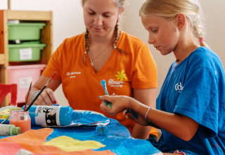 A child and an adult painting together at a table in Flower Camping Le Kerarno, Brittany, France.